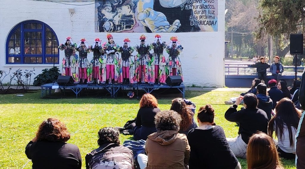 Fotografía de presentación de la murga La corre y vuela con personas mirándola, sentadas en los jardines