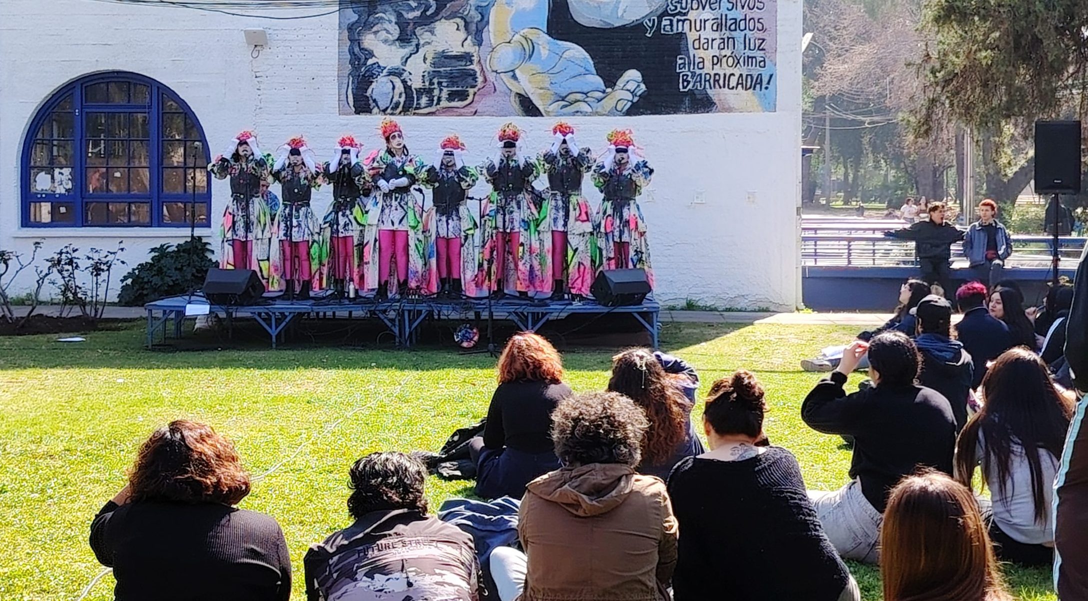 Fotografía de presentación de la murga La corre y vuela con personas mirándola, sentadas en los jardines