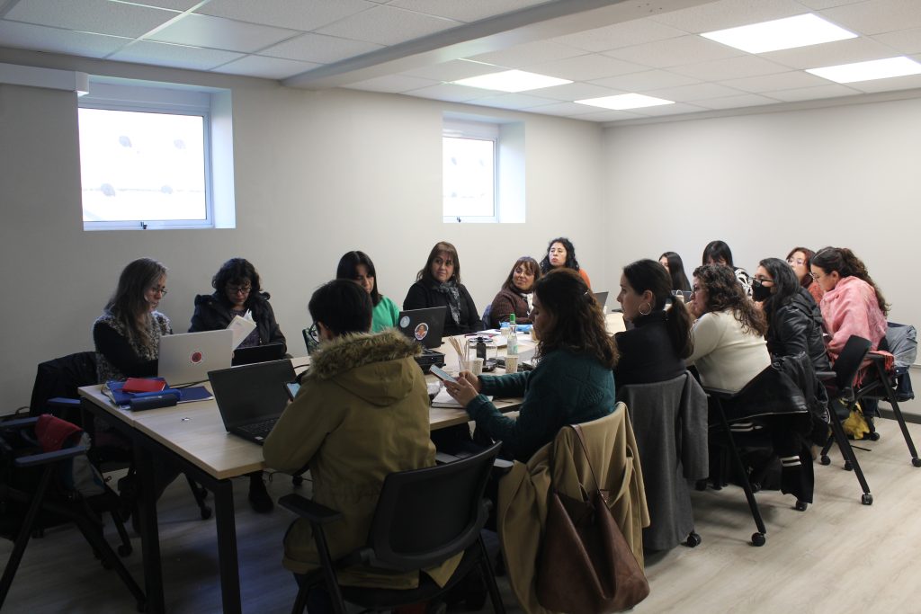 Fotografía de académicas sentadas en una mesa mirándose, durante el taller para guiar a académicas e investigadoras de la UMCE