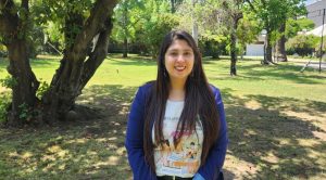 Pamela Palomera, directora del Depto. de Física, mirando a la cámara. De fondo, se ven jardines.