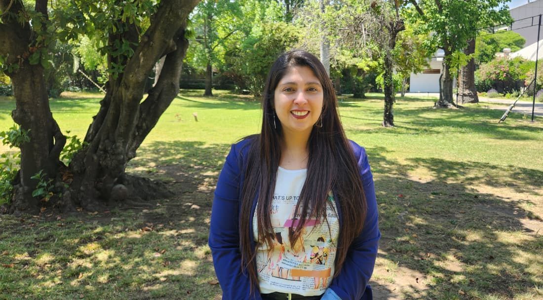 Pamela Palomera, directora del Depto. de Física, mirando a la cámara. De fondo, se ven jardines.